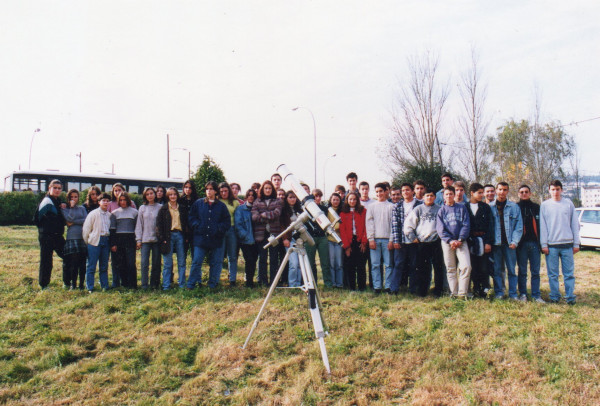 Alumnos da aula de astronomía posando detras do telescopio refractor nun terreo herboso.